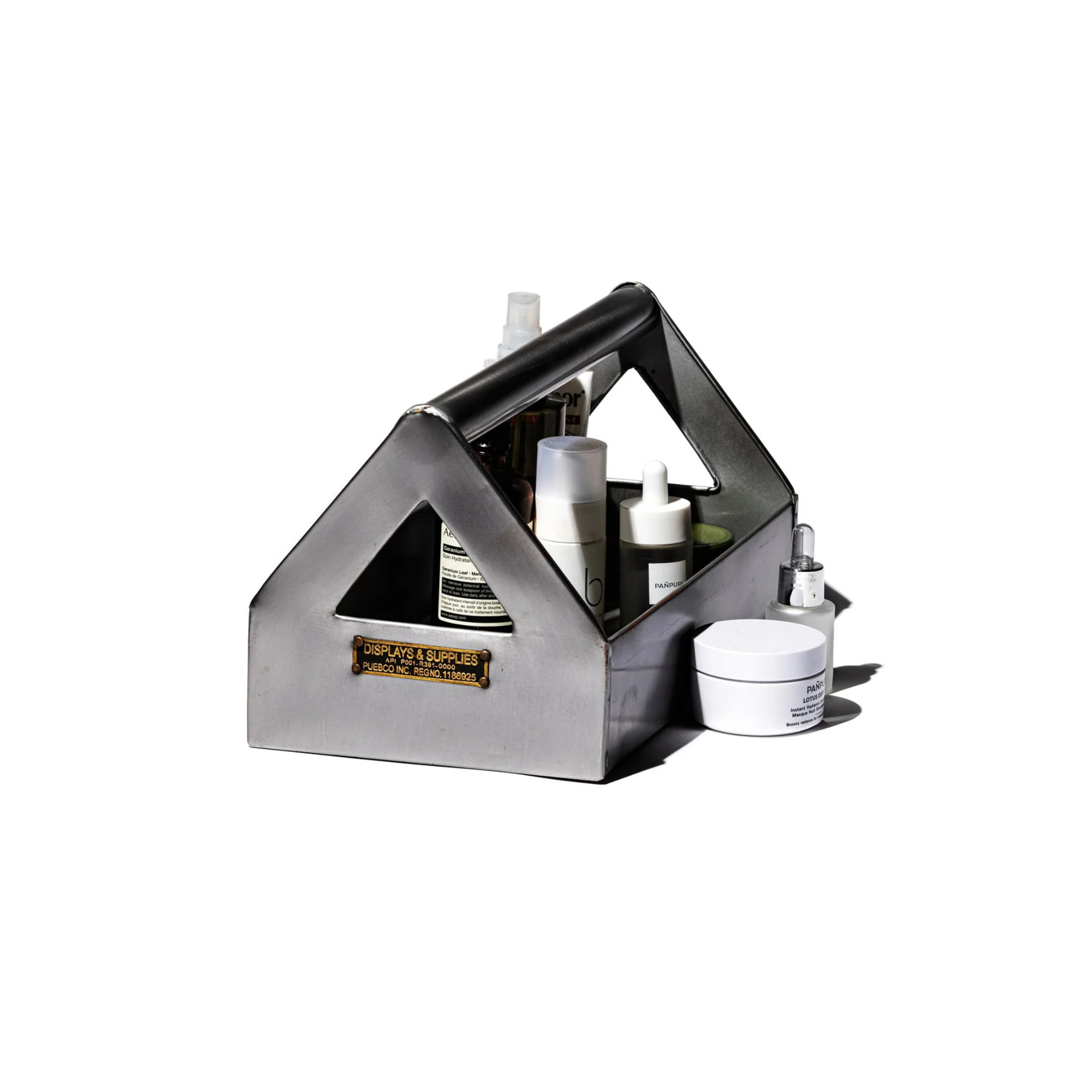 De Puebco Tool Organizer van Puebco, een metalen caddy met een handvat geïnspireerd op industrieel design, biedt plaats aan huidverzorgingsflesjes en -potjes, met twee extra containers ernaast op een witte achtergrond.