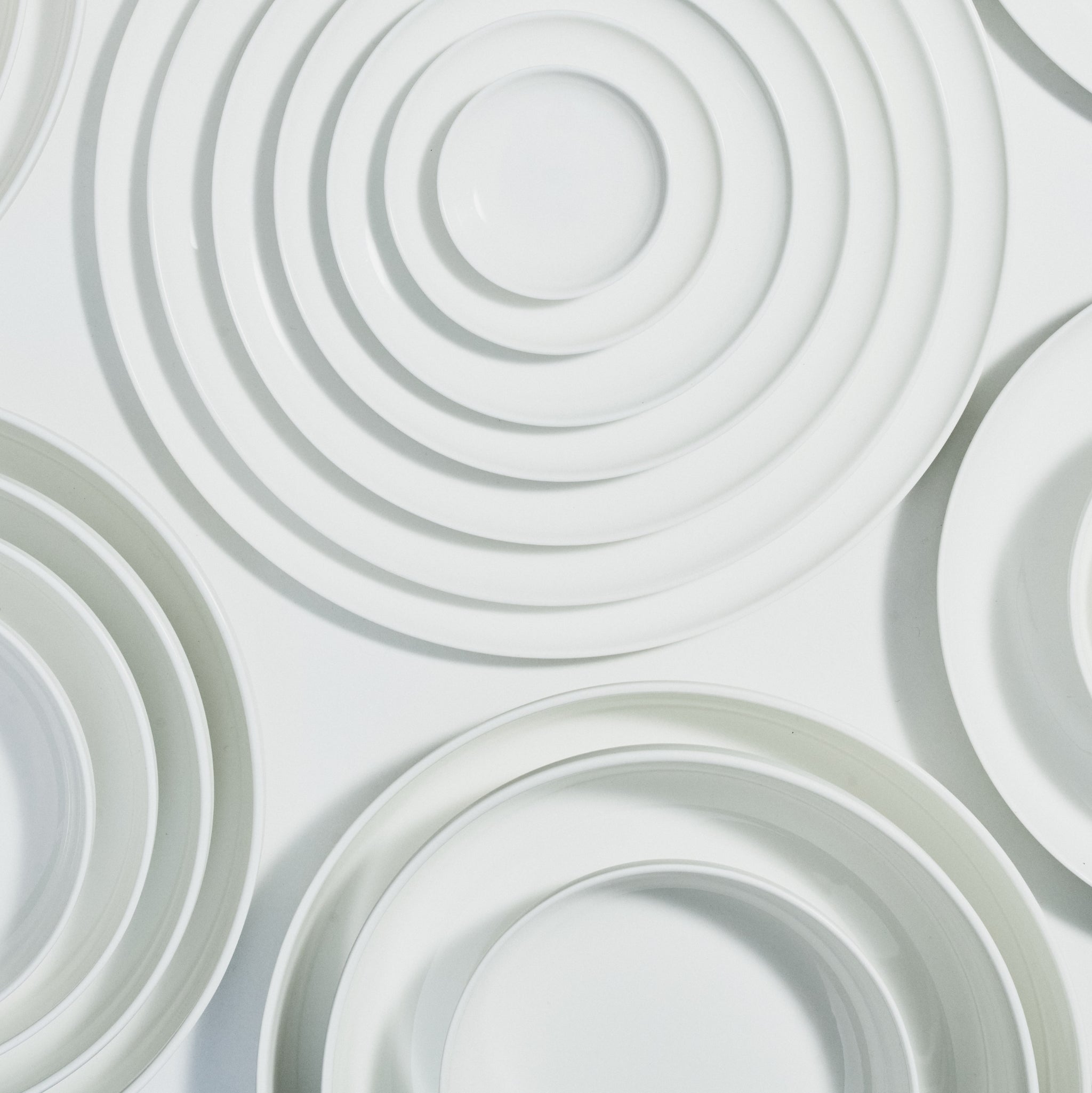 Een set witte Serax Base Diep Bord D16 borden, gerangschikt in overlappende cirkels op een witte achtergrond, doet denken aan de repeterende patronen van Piet Boon servies en Chinees porselein.