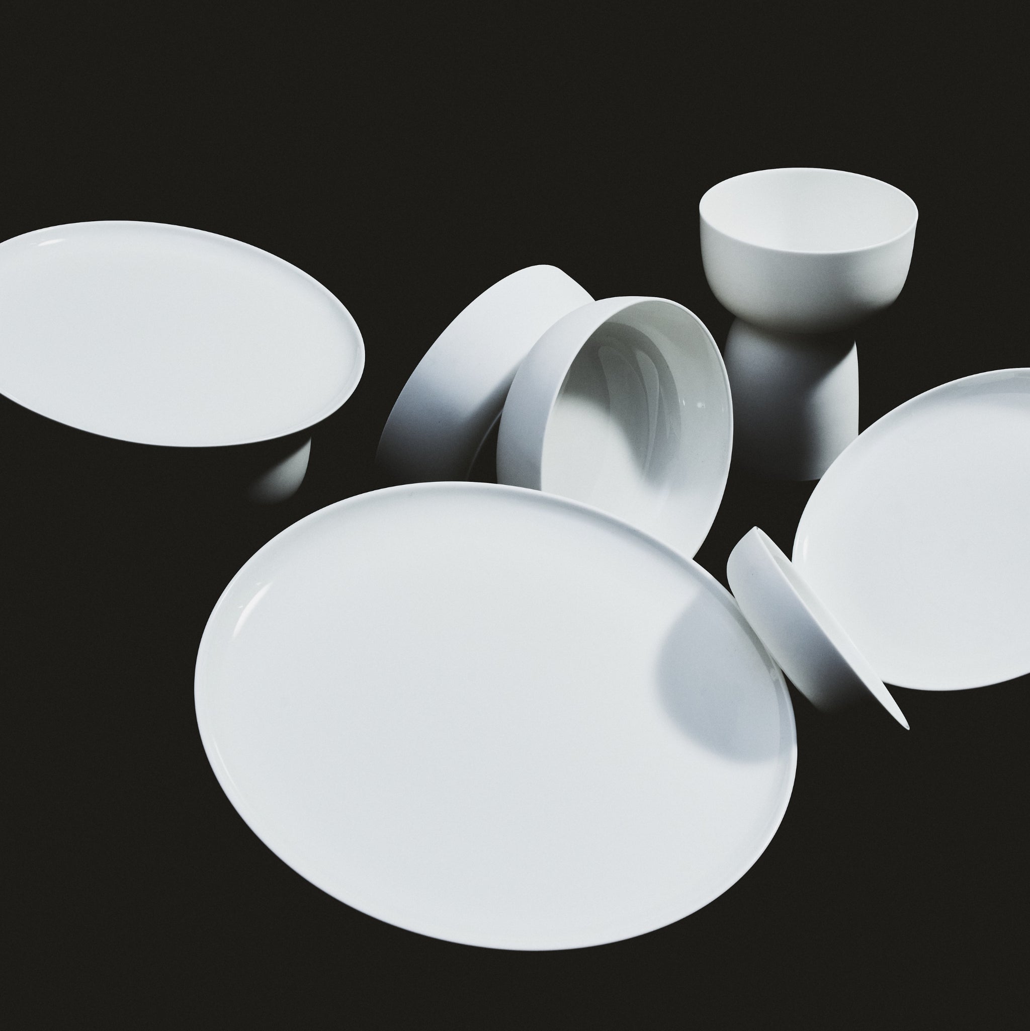 Een selectie Serax Base Laag Bord D32 keramische borden van Serax, gerangschikt op een zwarte achtergrond met sommige borden plat en andere gekanteld of gestapeld in verschillende hoeken.
