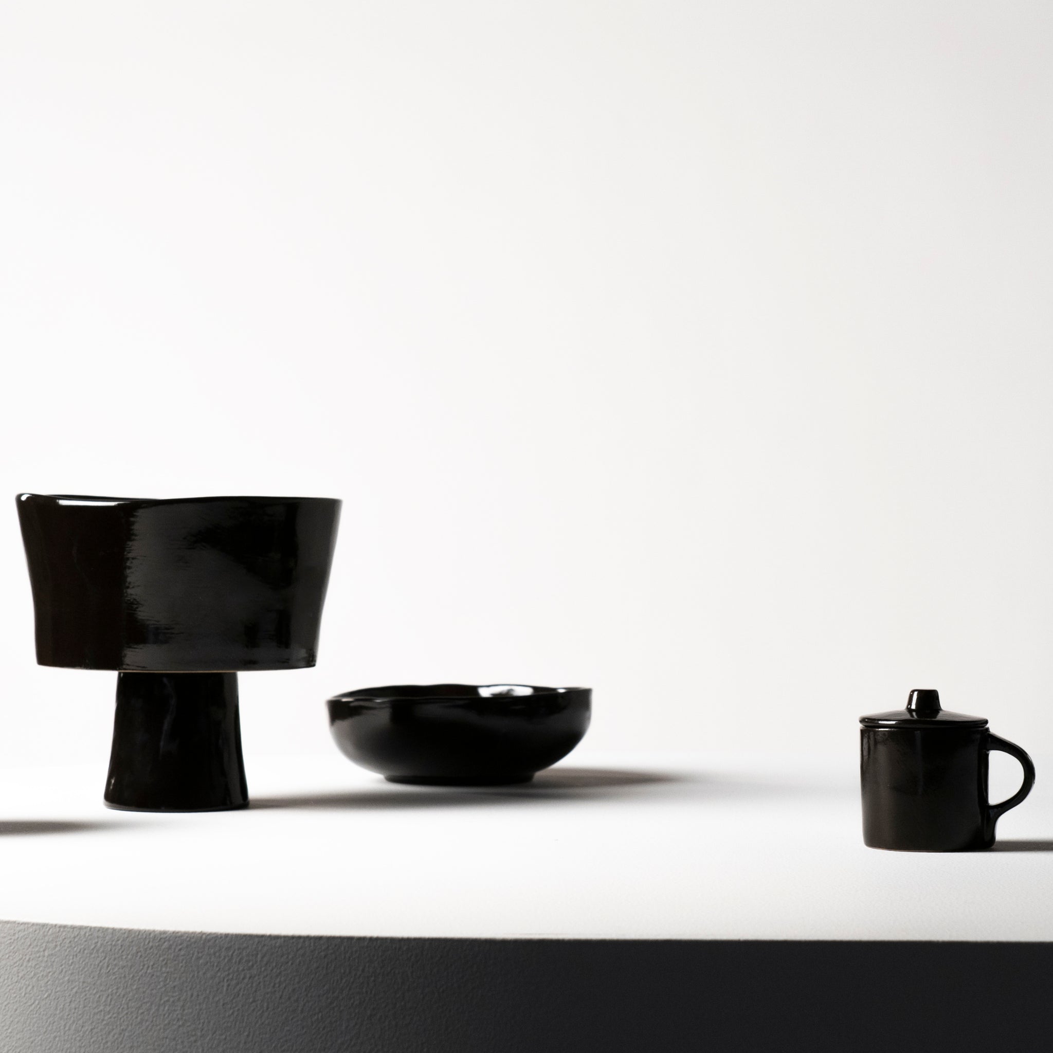 De Serax La Mère Serveerschaal Ebony D31 van Serax, een glanzend zwarte serveerschaal van keramiek, staat op een rond wit oppervlak tegen een effen witte achtergrond.