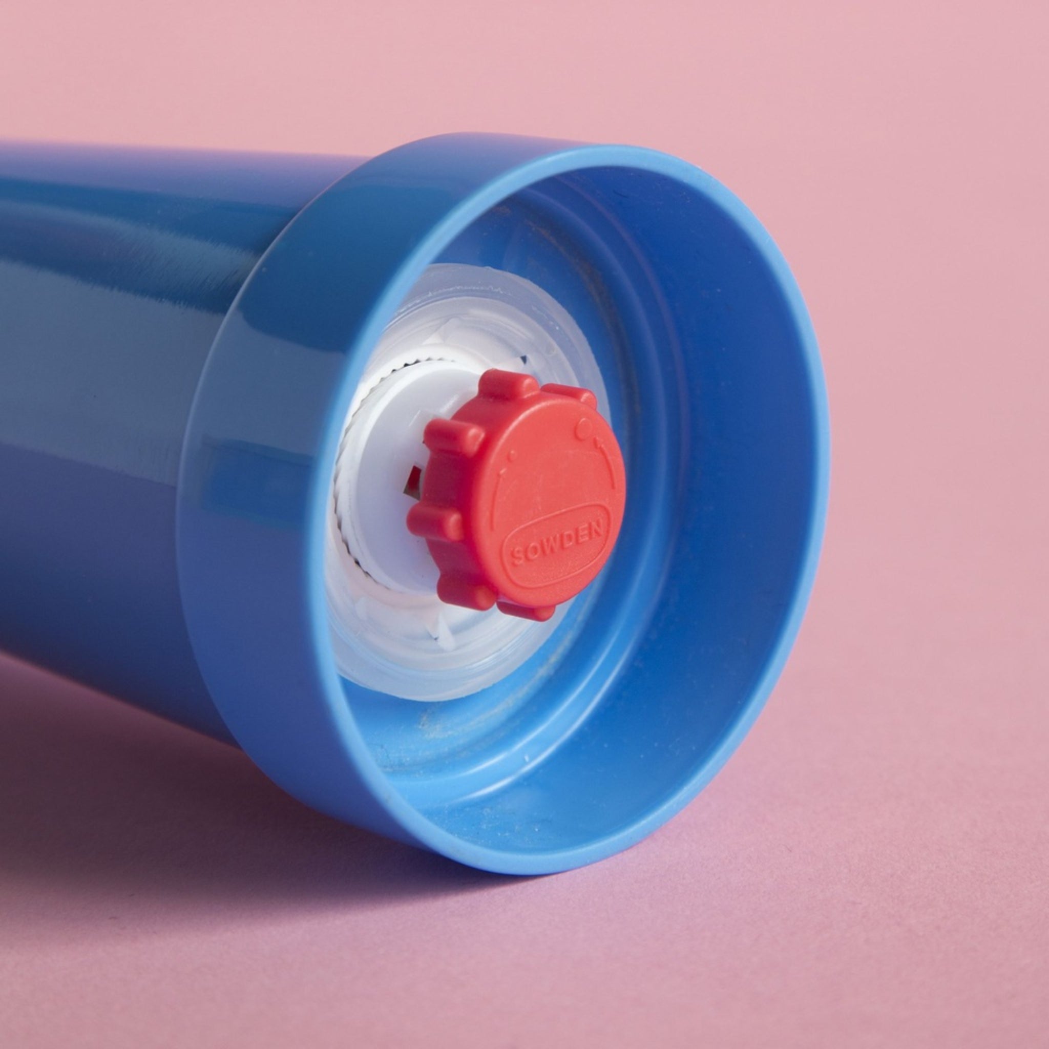 Een close-up van de blauwe Sowden Zout-en Pepermolen van Sowden, met een rode schroefdop en Memphis Design Movement inspiratie, rustend op een roze oppervlak.