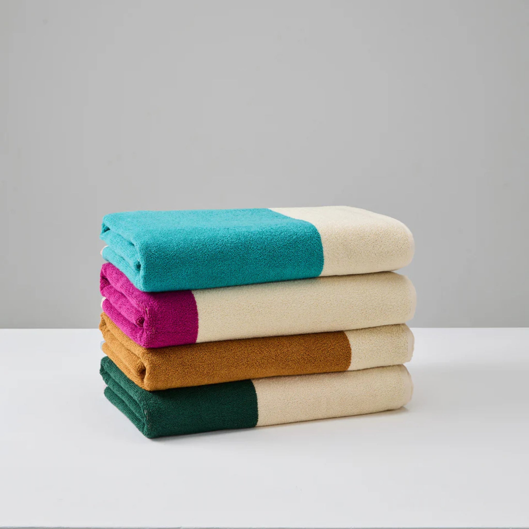 Een stapel van vier Suite 702 Badhanddoeken Rood Turquoise 70/140, gemaakt van biologisch katoen met color-block dessins, rust op een wit oppervlak tegen een effen lichtgrijze achtergrond.
