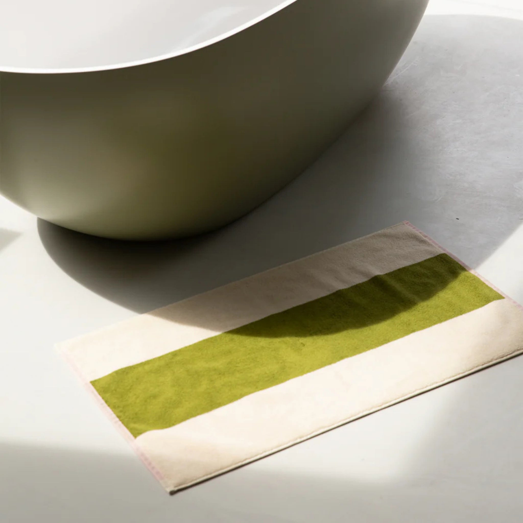 Naast de Suite 702 Badmat Roze Olijfgroen 50/80 van Suite 702 staat een modern bad met brede olijfgroene en beige strepen. Gemaakt van biologisch katoen voegt het elegantie toe aan de lichtgekleurde vloer.