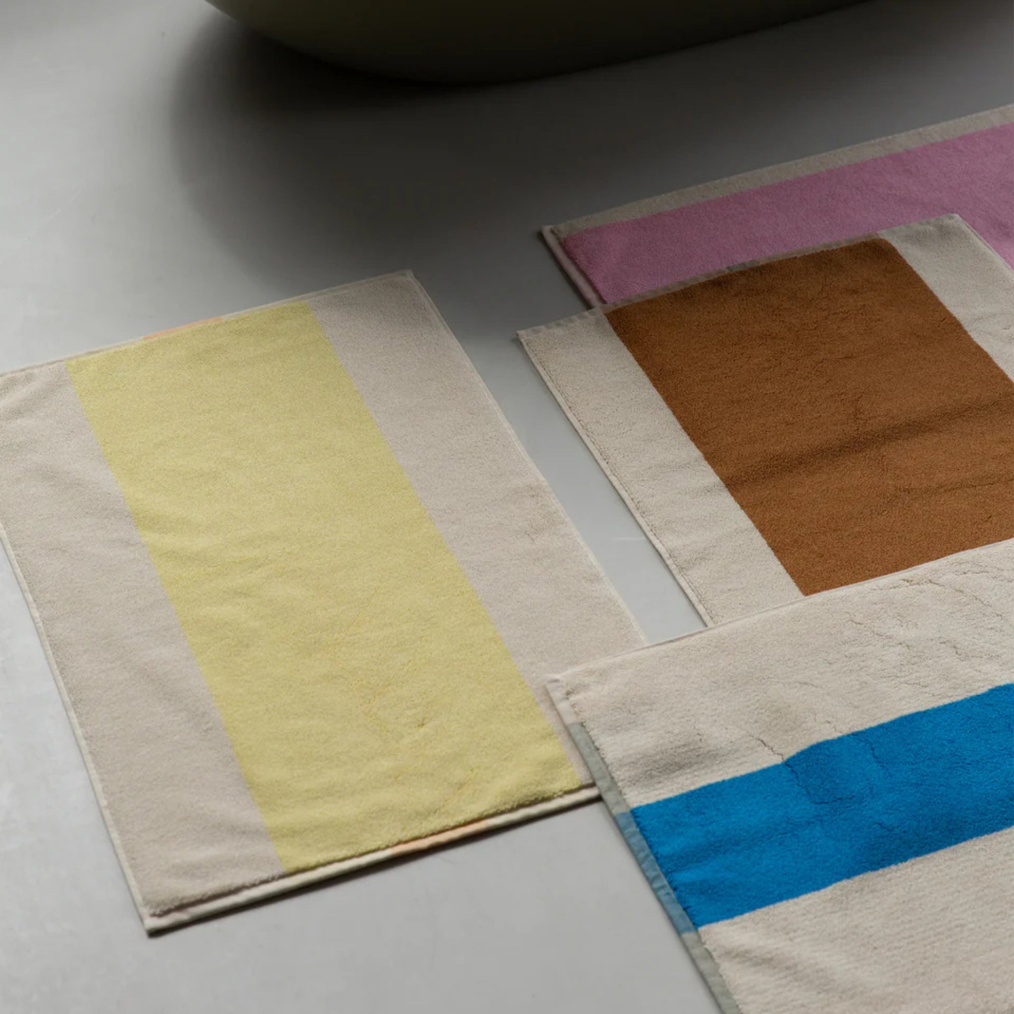 De Suite 702 Badmat Aqua Donkergroen 50/80 van Suite 702, gemaakt van biologisch katoen, heeft een minimalistisch ontwerp met gedurfde strepen in geel, bruin, roze en blauw - een moderne, op Karel Martens geïnspireerde touch voor elke lichtgekleurde vloer.