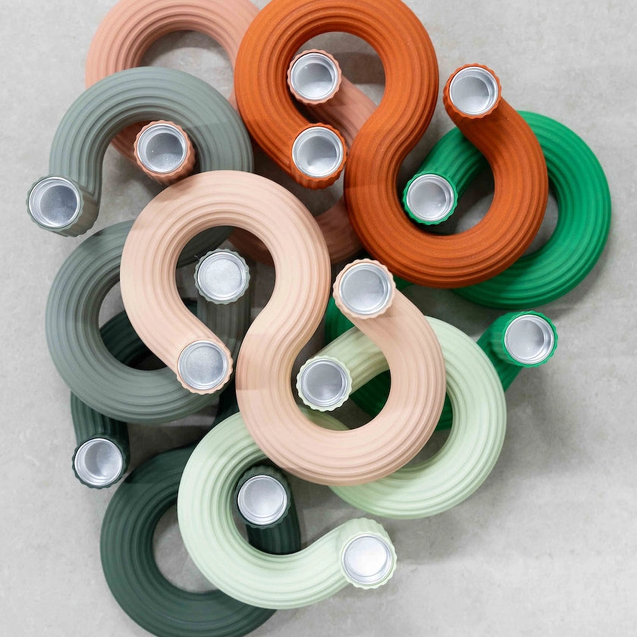 Gebogen waterflessen in groen, beige, oranje en grijs overlappen elkaar op een licht oppervlak. Hun geribbelde vormen en zilveren doppen weerspiegelen de abstracte look van Wavy Kandelaar Rood van Wavy Design Studio.