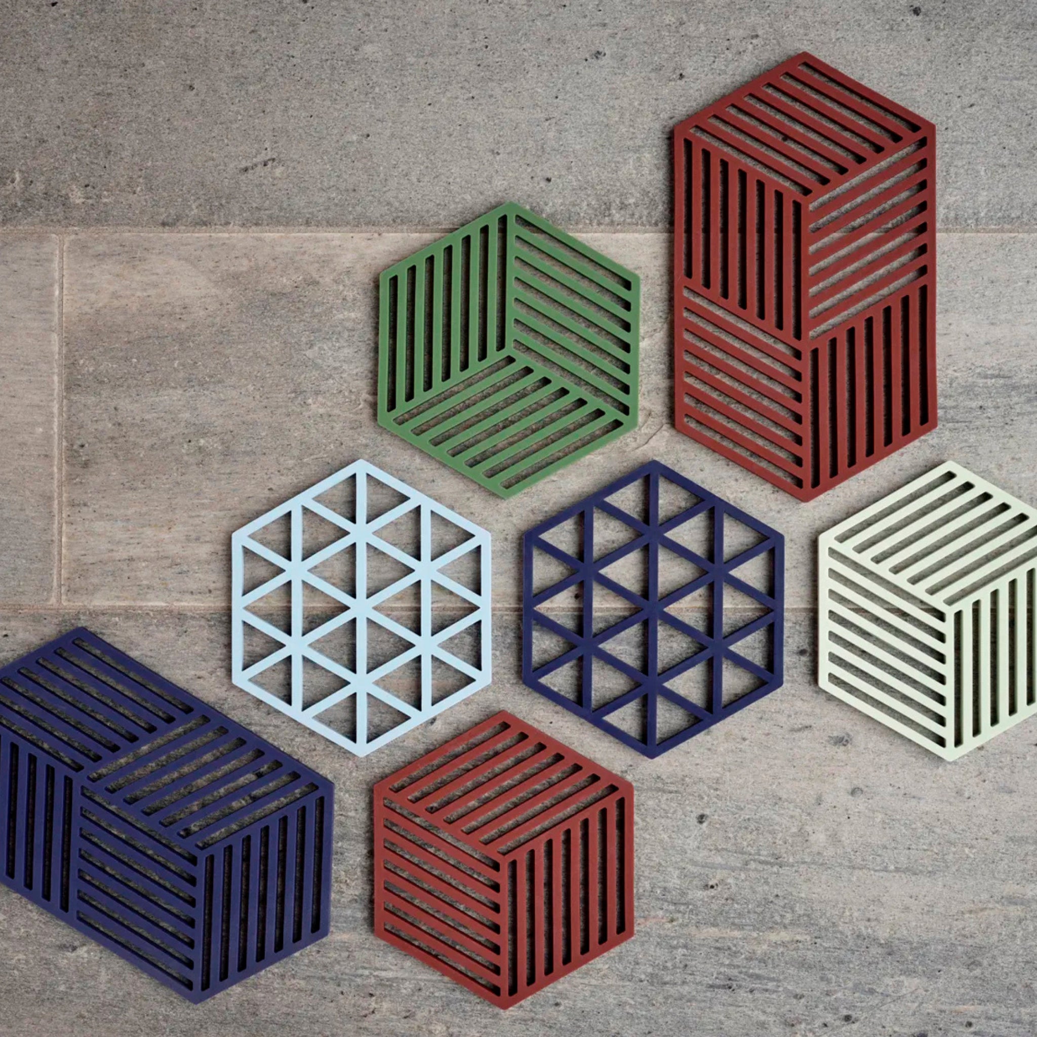 De Zone Denmark Triangles Trivet Indigo van Zone Denmark heeft een geometrisch uitgesneden patroon met driehoeken en voegt moderne stijl toe aan je tafelsetting. Afgebeeld op steen, benadrukt het de kenmerkende esthetiek van het merk in opvallend indigo.