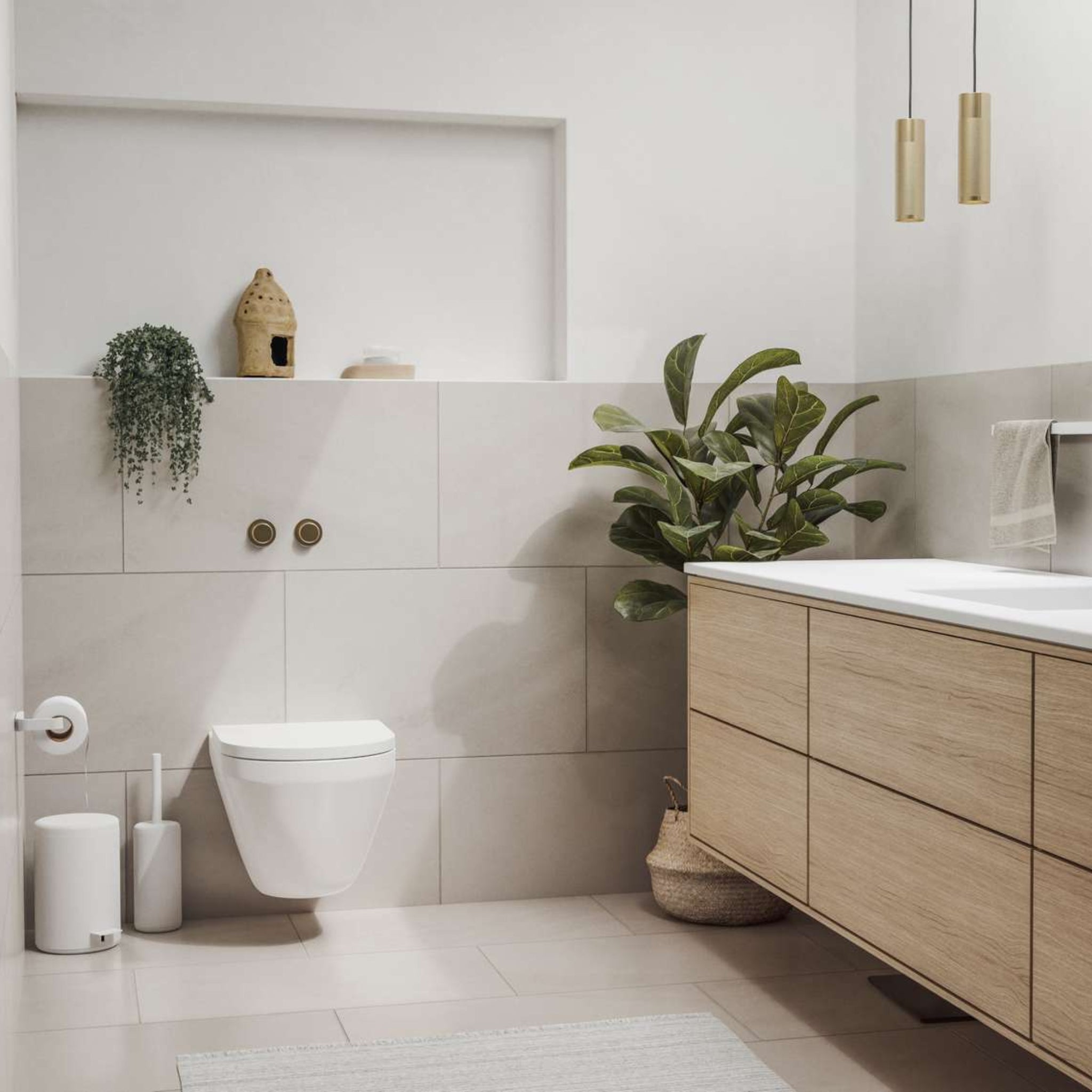 Een moderne badkamer met een zwevend toilet, een licht houten badmeubel, een groene plant in mandjes en een Zone Denmark Rim Toiletborstel Wit op een richel aan de muur met decor. De ruimte is licht, neutraal en minimalistisch ingericht.