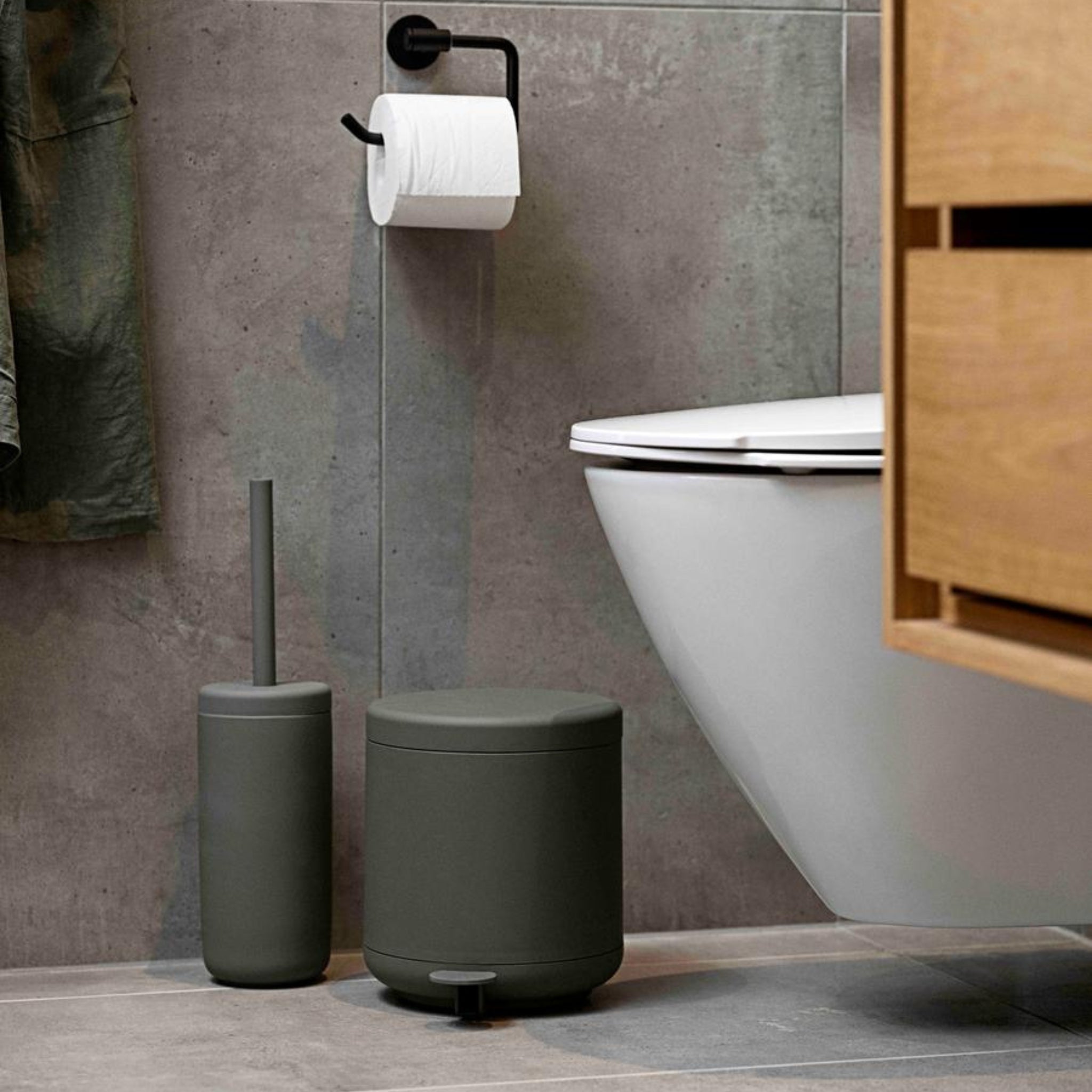 Moderne badkamer met de Zone Denmark Ume Toiletborstel Olijfgroen, een zwarte pedaalemmer en toiletpapier op een zwarte houder - de strakke badkameraccessoires van Zone Denmark steken mooi af tegen de grijs betegelde muren.