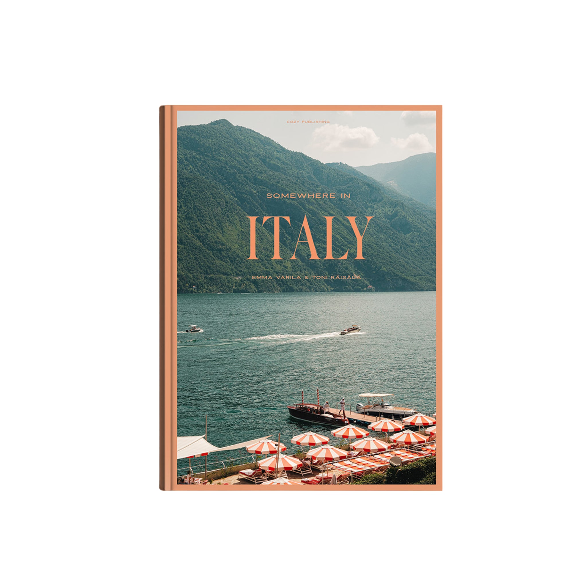 De Cozy Publishing Somewhere in Italy Reisgids van Cozy Publishing nodigt je uit om verborgen parels in schilderachtige Italiaanse regio's te verkennen, met een omslag waarop boten, weelderig groene bergen en rood-wit gestreepte paraplu's bij een meer zijn afgebeeld.