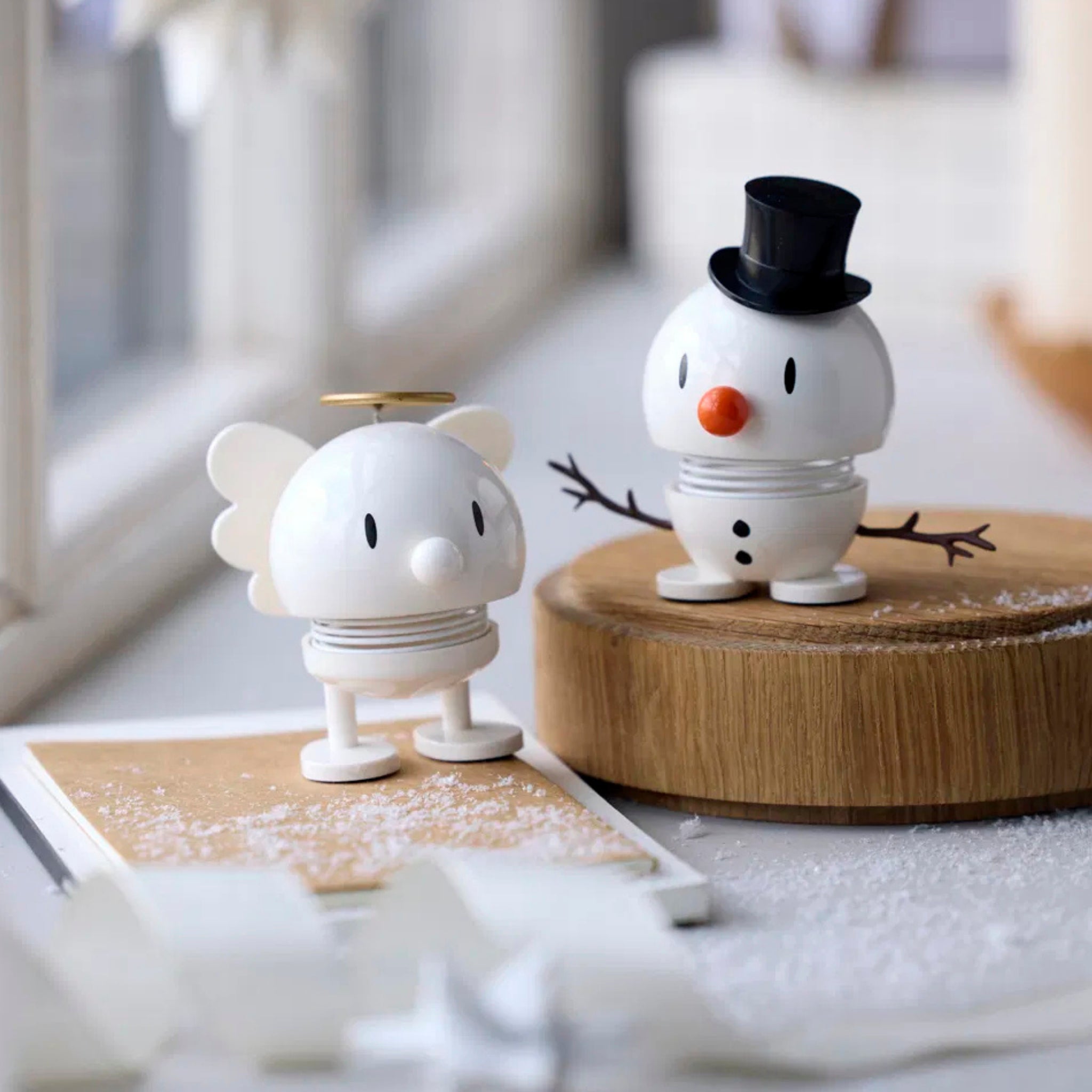 De Hoptimist Sneeuwman Bumble S Wit van Hoptimist is een charmant wit beeldje dat lijkt op een sneeuwpop met een hoge hoed, staand op een houten oppervlak met sneeuwachtige poeder-perfecte kerstdecoratie en een ideaal cadeautje voor elke feestelijke omgeving.