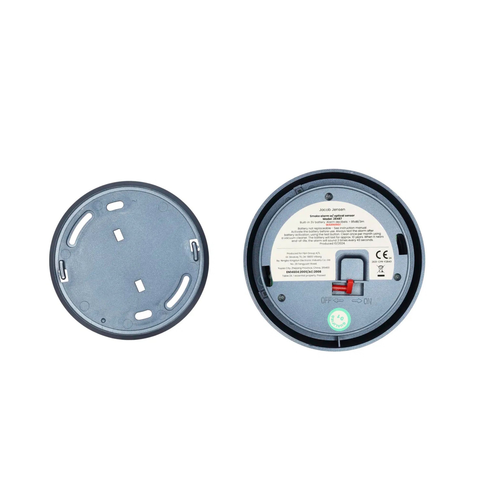 Twee ronde apparaatvoeten naast elkaar: de ene is een Jacob Jensen Optical Rookmelder Blauw D10 met etiket, schakelaars en groene indicator; de andere toont alleen de effen koperen onderkant met sleuven. Merk: Jacob Jensen.