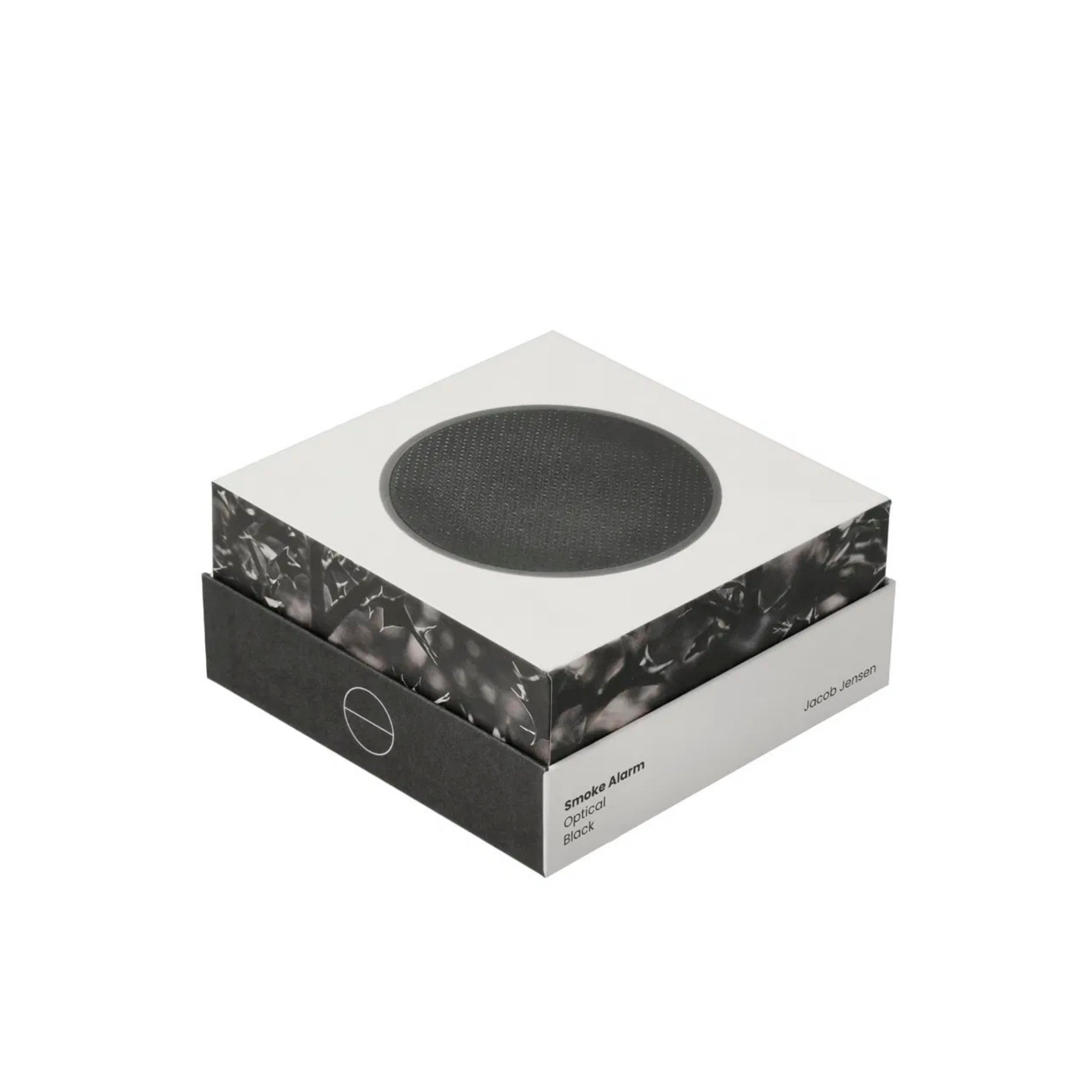 Een moderne vierkante doos toont een cirkelvormig zwart apparaat op het deksel, met het label Jacob Jensen Optical Rookmelder Zwart D10, een strakke zwart-witte rookmelder geïnspireerd op het minimalistische ontwerp van Jacob Jensen.