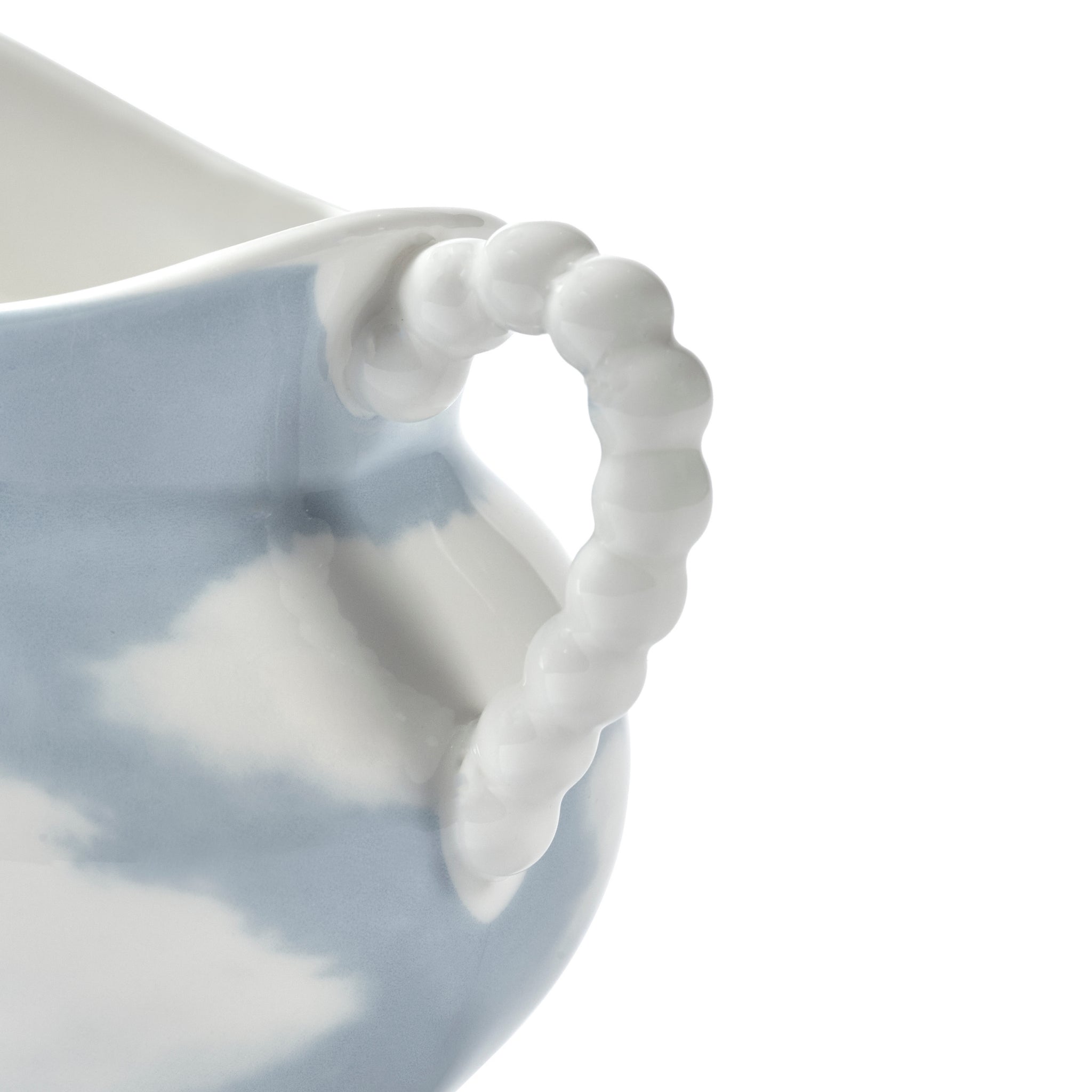 Close-up van het Serax Wouters & Hendrix Fête Des Bêtes Melkkannetje Lichtblauw, met een blauw-wit wolkenpatroon en een wit handvat met textuur en kralen, tegen een effen witte achtergrond.