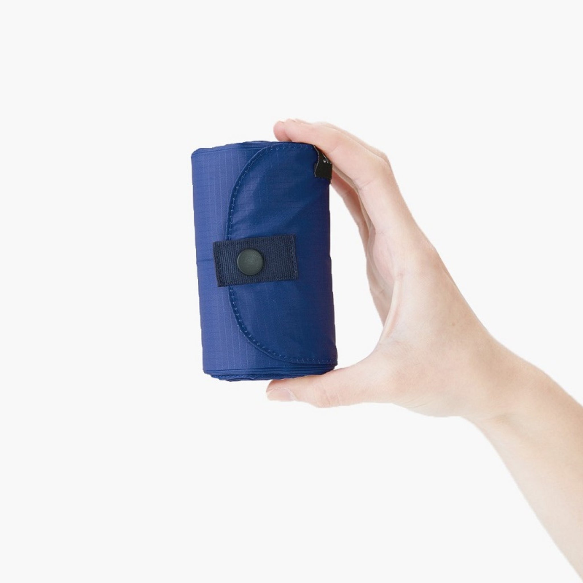 Een hand houdt een Shupatto Opvouwbare Boodschappentas Donkergroen L met drukknoopsluiting vast, opgerold tegen een effen witte achtergrond.