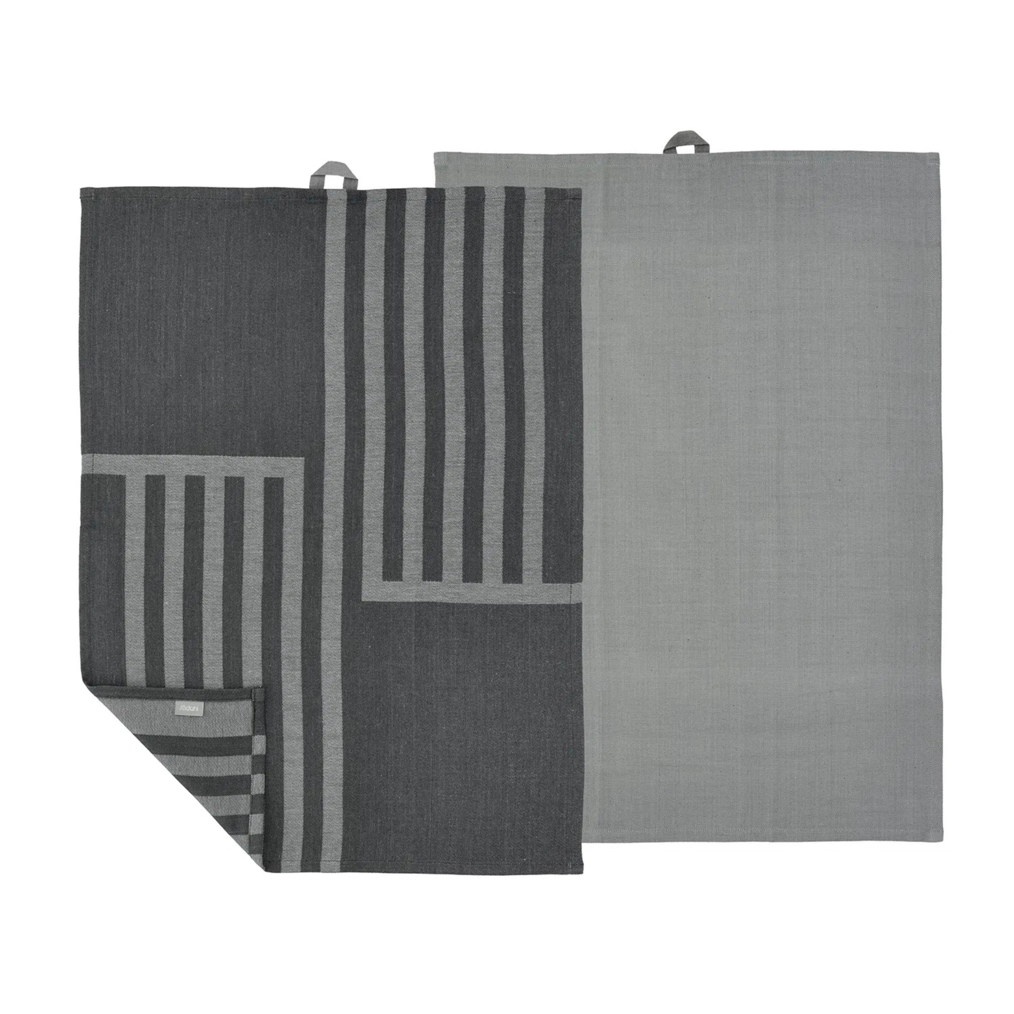 Set van twee Södahl Reflection Theedoek Ash: een effen lichtgrijze, de andere donkergrijs met lichtgrijze strepen in een geometrisch Scandinavisch patroon. Beide hebben ophanglussen; de gestreepte handdoek is gedeeltelijk gevouwen aan één hoek.