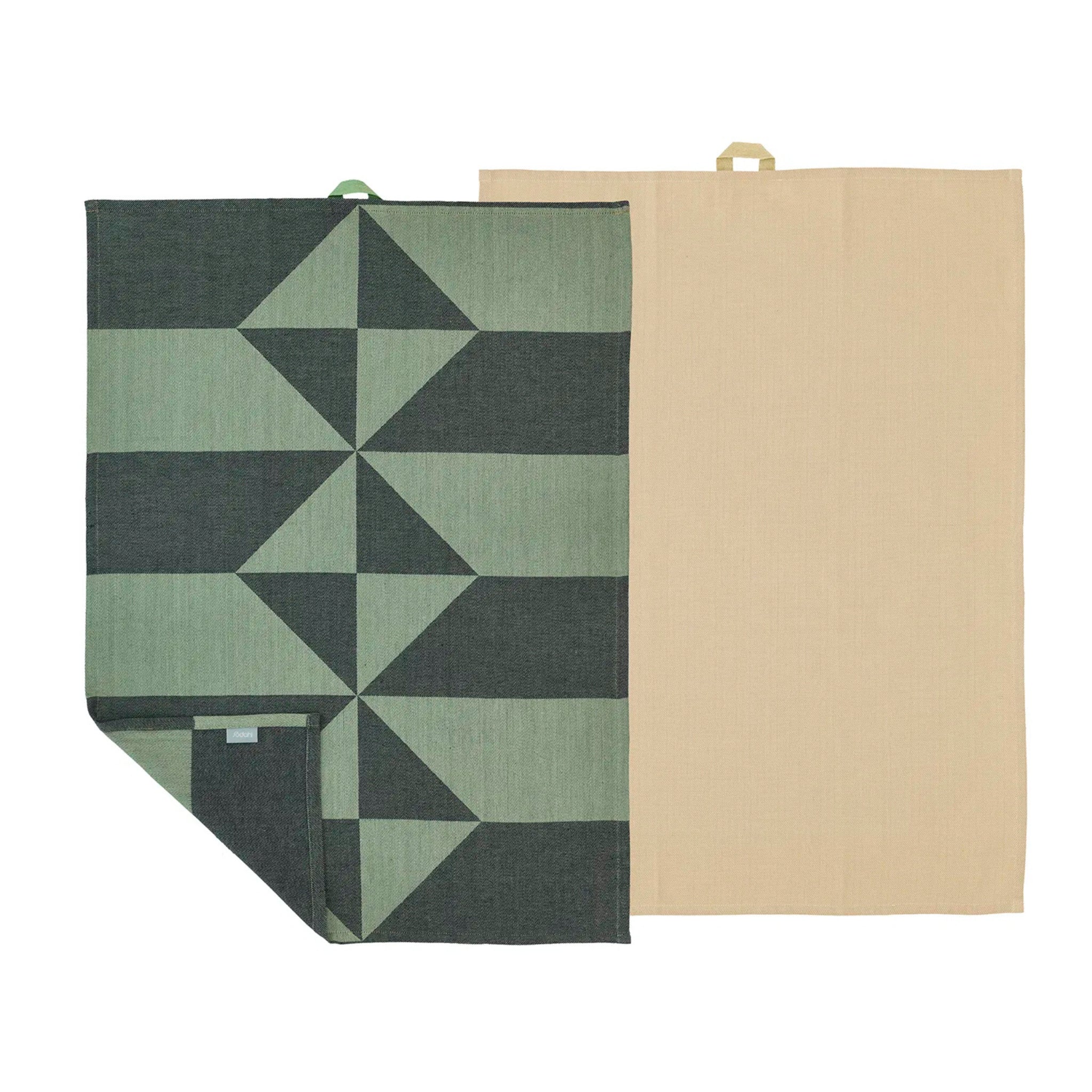 Twee Södahl Twist Theedoek Groen 2 st. theedoeken liggen naast elkaar: een met een donker en lichtgroen geometrisch patroon, de ander effen beige. Beide Scandinavische keukendoeken hebben stoffen lussen om ze gemakkelijk op te hangen aan de bovenkant.