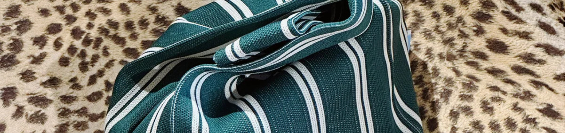 Een groen-wit gestreepte stoffen tas ligt op een oppervlak met een luipaardprintpatroon op de achtergrond.