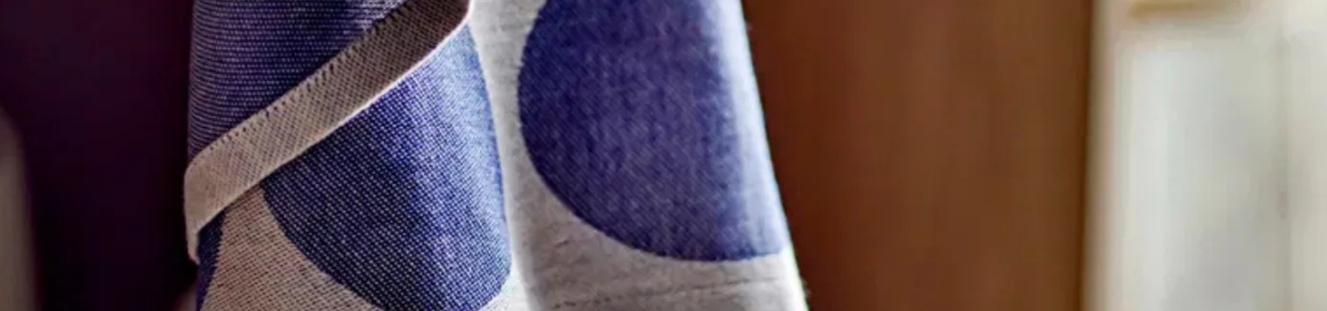 Een close-up van een stof met een gedurfd blauw cirkelpatroon op een lichtgrijze achtergrond, met een zacht vage bruine achtergrond. De textuur van de stof is duidelijk zichtbaar.