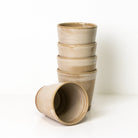 Vijf AB Ceramics Beker Toffee Satijn bekers van 20 cl zijn verticaal gestapeld, met één beker horizontaal liggend aan de basis voor de stapel. Alle kopjes van AB Ceramics staan tegen een effen witte achtergrond.