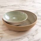Twee AB Ceramics Serveerschalen Ruw Mint D27,5 zijn genest op marmer; de kleinste heeft een lichtgroene binnenkant, terwijl de grootste beige is met een natuurlijke, ongeglazuurde afwerking.