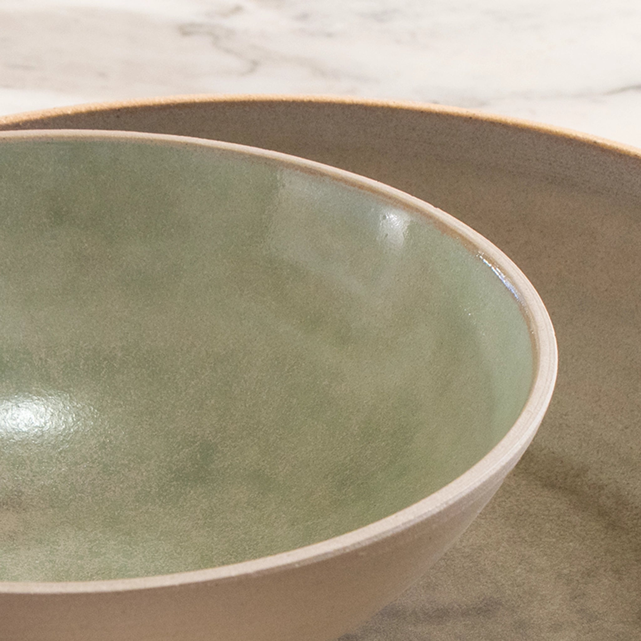 Close-up van twee keramische kommen op een licht marmeren oppervlak, met de AB Ceramics Noodle Kom Wit Mint D19 met een glanzende lichtgroene binnenkant en een matbeige noodle bowl.