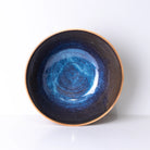 De AB Ceramics Serveerschaal Geel Blauw D23 is een ronde handgemaakte keramieken schaal met glanzend blauw-geel interieur en matte bruine buitenkant, van het merk AB Ceramics, afgebeeld tegen een witte achtergrond.