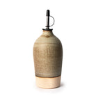 De AB Ceramics Olijfolie Fles 2 Wit Mos 55 cl van AB Ceramics is een handgeblazen oliedispenser van keramiek in mat beige en bruin, met een metalen schenktuit met zwarte dop - een elegant keukenaccessoire dat rechtop staat op een witte achtergrond.