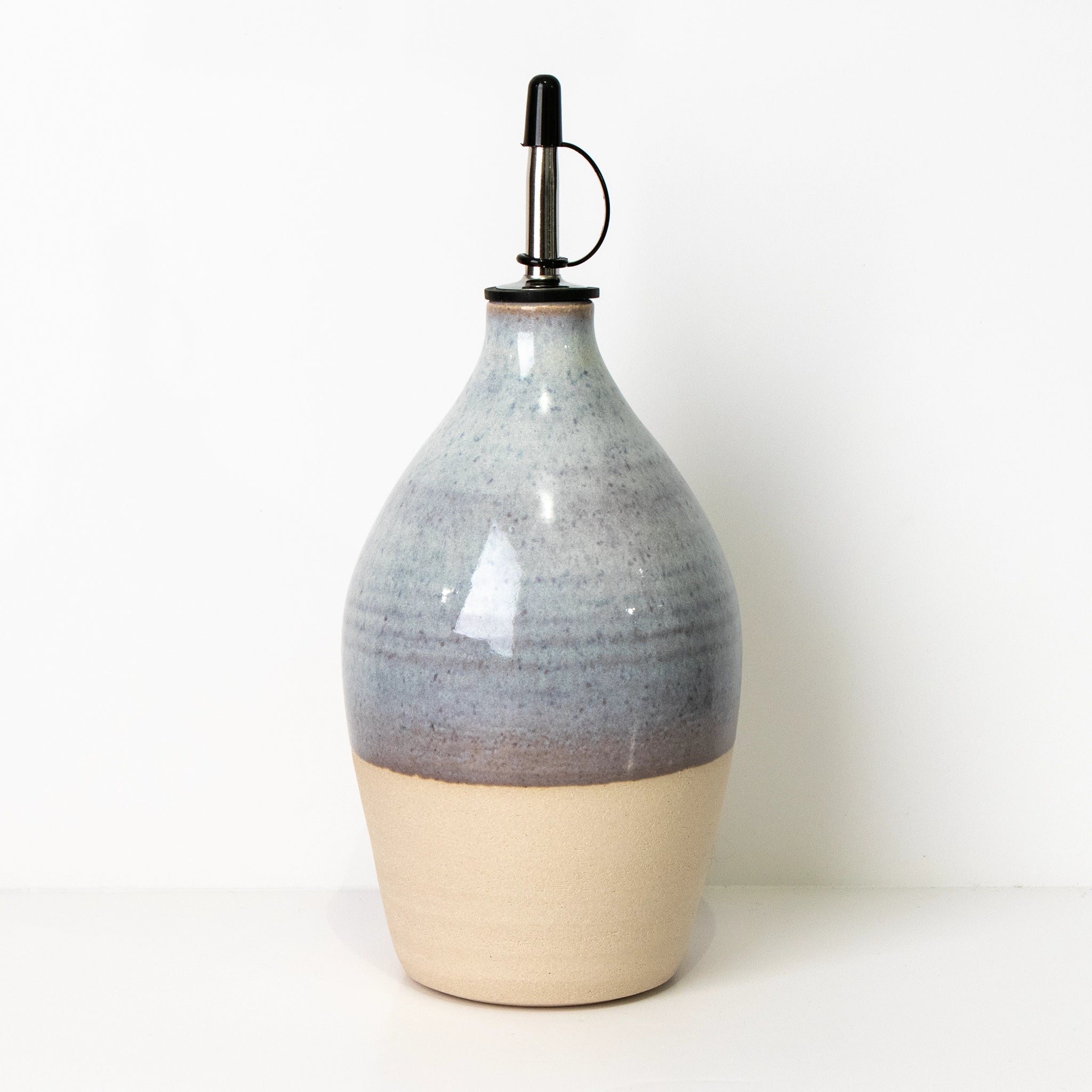 De AB Ceramics Olijfolie Fles Wit Opaal 85 cl is een handgedraaide keramische fles met glanzende blauwgrijze bovenkant en metalen schenktuit, een stijlvolle keukenaccessoire van AB Ceramics op een witte achtergrond.