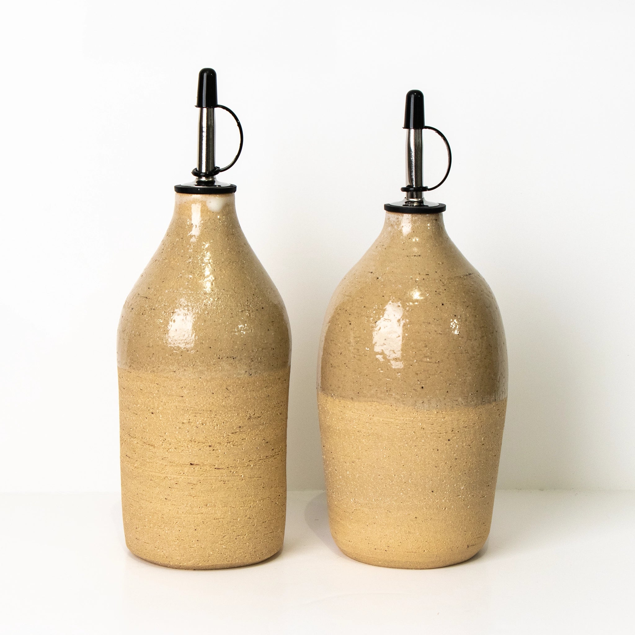 Twee AB Ceramics Olijfolie Fles Ruw Transparant 60 cl dispensers, met zwarte schenktuiten en lussen, zijn naast elkaar geplaatst tegen een effen witte achtergrond.