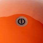 Een close-up van het oppervlak van een oranje lamp met een rond symbool van een aan/uit-knop in het midden, wat het strakke ontwerp oproept van de Addison Ross Bobbin Lamp LED Oplaadbaar Oranje van Addison Ross.