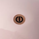 Een close-up van een zwart machtssymbool als een verticale lijn in een cirkel op lichtroze, perfect passend bij de zachte gloed van sfeerverlichting of de Addison Ross Bobbin Lamp LED Oplaadbaar Roze.