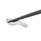 Een paar Alessi Anna eetstokjes rust op een slanke, zilveren vogelvormige houder tegen een witte achtergrond - een elegant tafelaccessoire van Alessi.