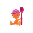 Het Alessi Cico Eierdopje Roze van Alessi heeft een oranje cartoonfiguurtje met een roze muts en bijpassende lepel, geïnspireerd op Italiaans design en afgebeeld tegen een effen witte achtergrond.