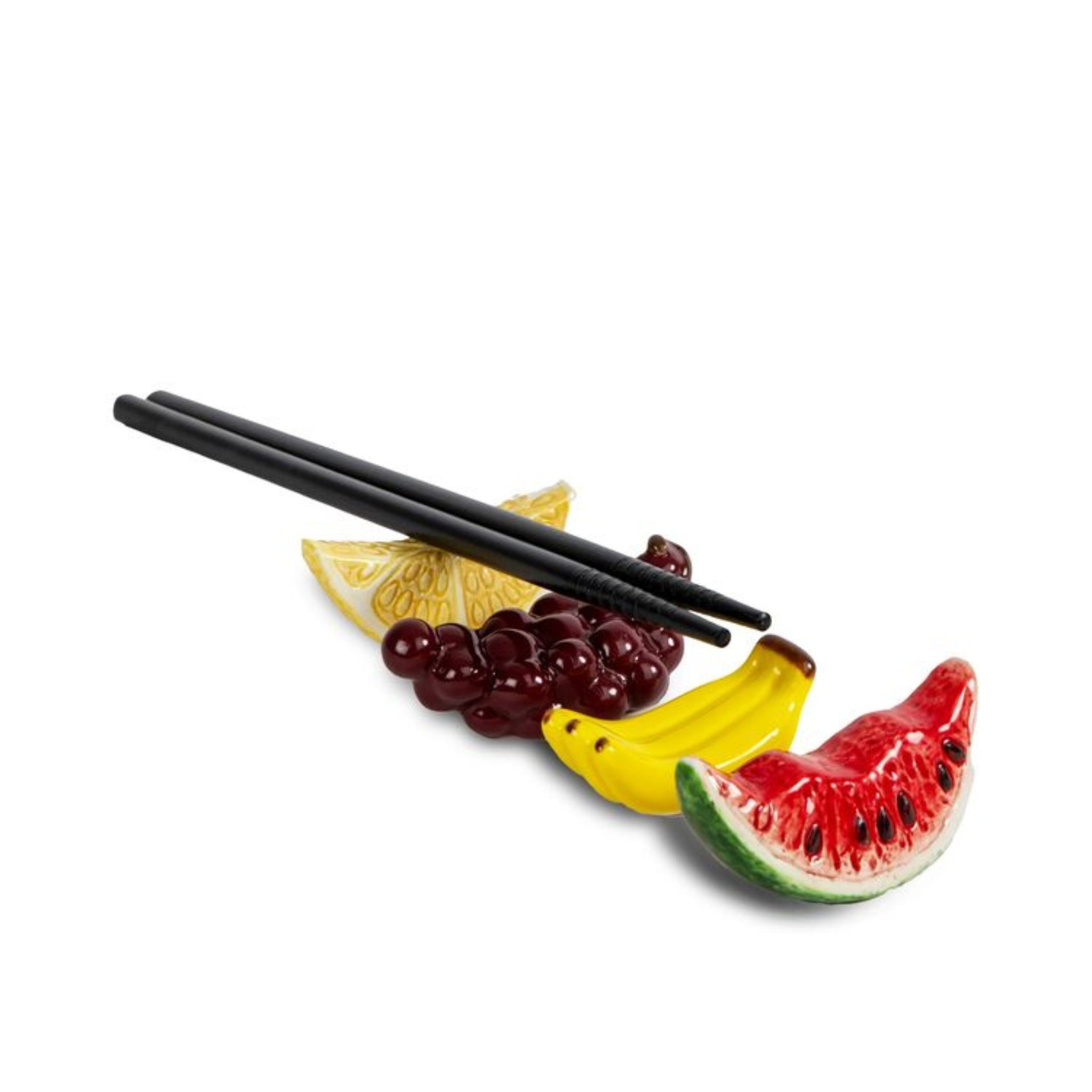 Een paar Byon Yaki eetstokjes rust op keramische eetstokhouders in de vorm van watermeloen, bananen, druiven en een citroen - een opvallende geschenkset op een witte achtergrond.