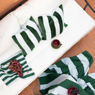 Een witte buitenbank met gestreepte kussens, een bijpassende deken, de Byon Pathi Kussen Groen/Blauw 45/45, een doek met druivenpatroon en een rode glazen beker staan op terracotta tegels.