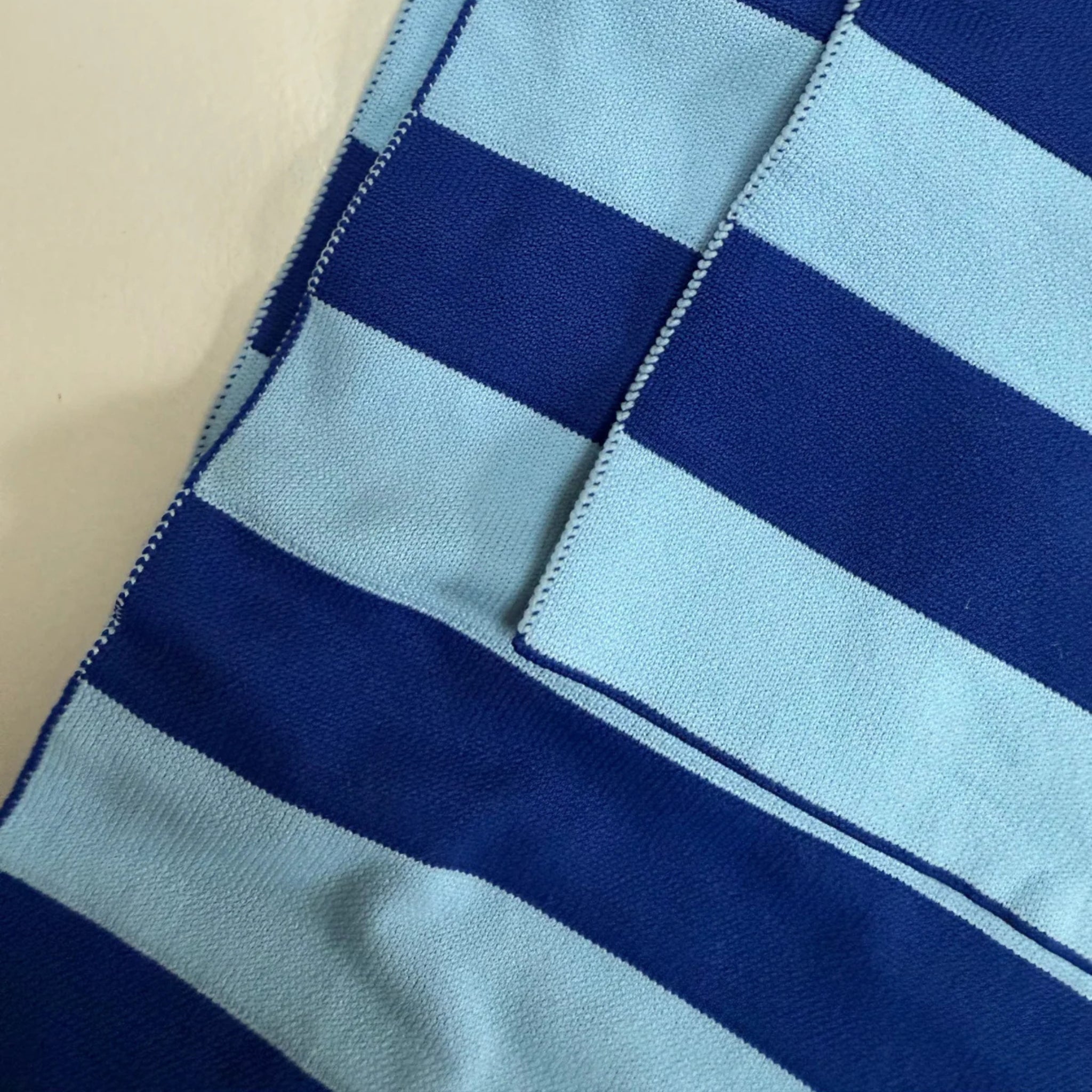 Close-up van blauwe en lichtblauwe horizontaal gestreepte stof met zichtbare stiksels, naden en zakdetails - perfect om te combineren met de Caro Antwerp Caro Sjaal Ace Ice Ice Baby.