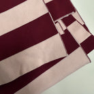 Een close-up van de gevouwen Caro Sjaal Ace Pinky Promise van Caro Antwerp toont brede horizontale kastanjebruine en lichtroze strepen met netjes gestikte randen.