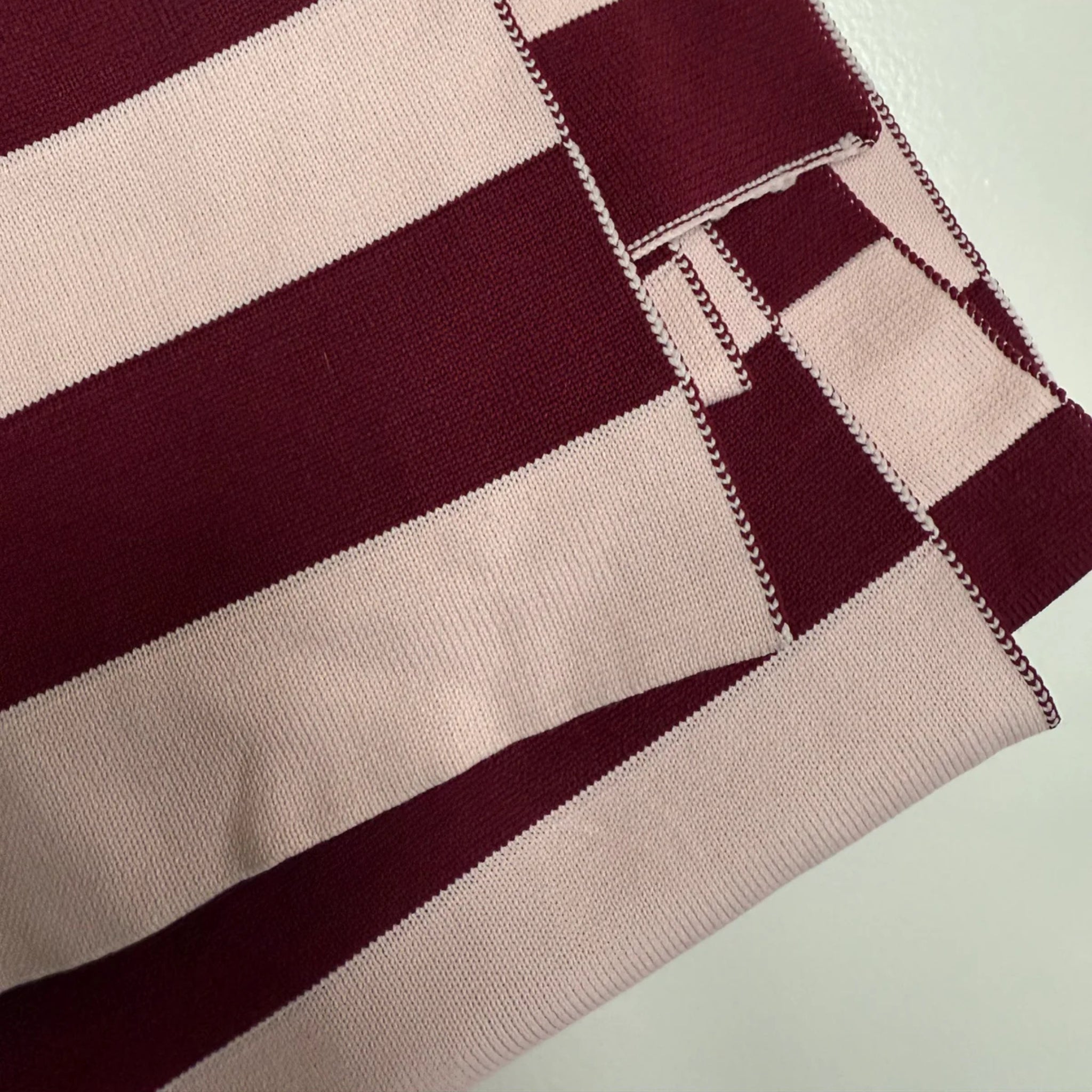 Een close-up van de gevouwen Caro Sjaal Ace Pinky Promise van Caro Antwerp toont brede horizontale kastanjebruine en lichtroze strepen met netjes gestikte randen.