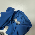 Een Caro Antwerp Caro The Scrunch Club Scrunchie 2 st. in blauw met een reflecterende afwerking rust op een licht oppervlak, de zachte plooien vormen een ongelijke cirkel-ideaal als een trendy fiets accessoire voor extra zichtbaarheid.