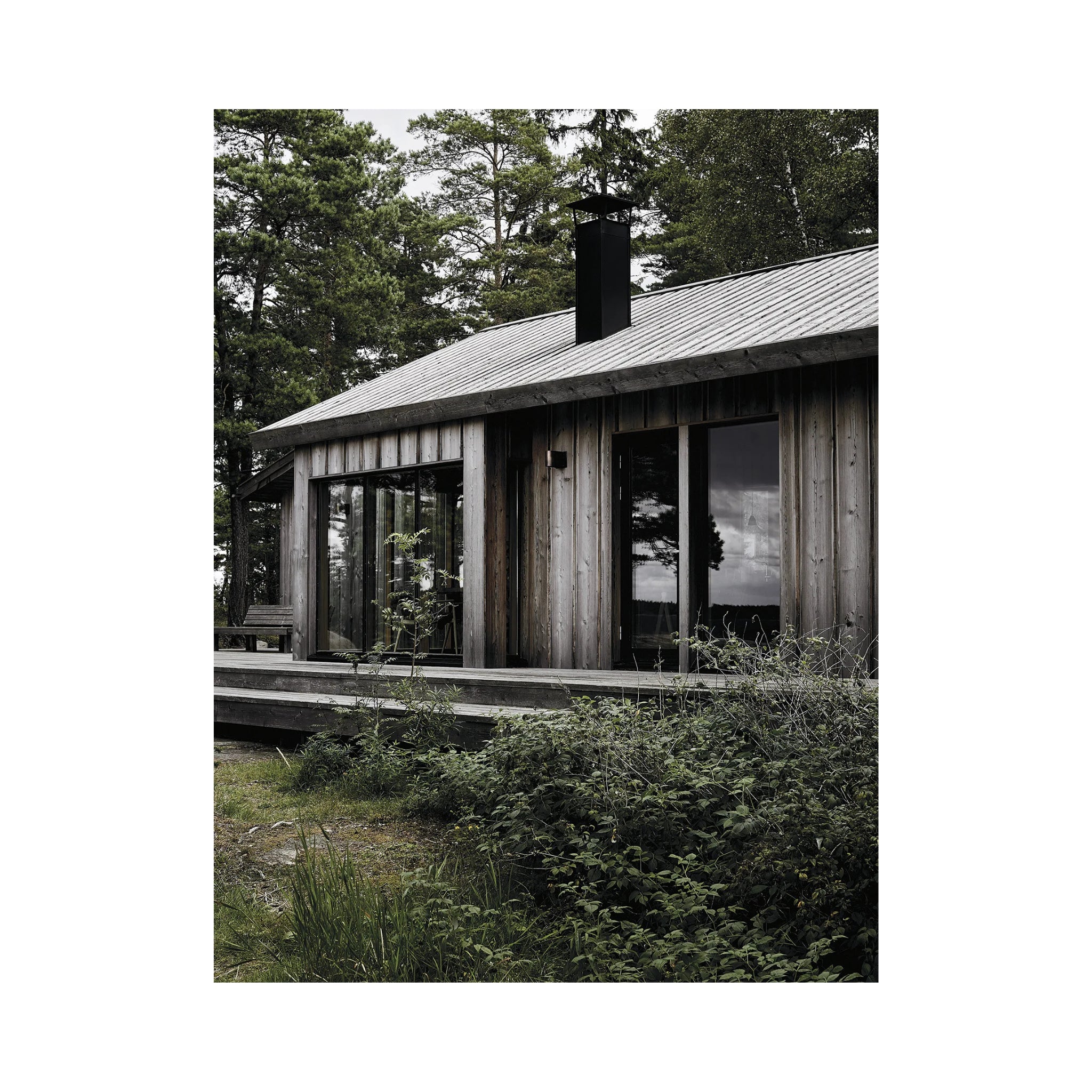 Een moderne houten hut met grote ramen en een metalen schoorsteen staat op een dek tussen hoge bomen, zoals te zien is in het boek Happy Homes Hideaways van Cozy Publishing.