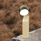 Een moderne Fine Lumens Mono Leeslamp LED Oplaadbaar in olijfgroen en geel staat buiten op een betonnen oppervlak, met droog bruin gras op de achtergrond.