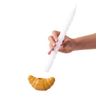 Een hand houdt een lange, gedraaide witte kaars vast boven de Fluid Market Croissant Kandelaar van Fluid Market, een unieke kandelaar van keramiek tegen een effen witte achtergrond.