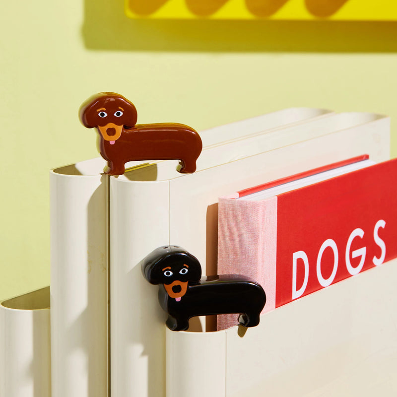 De Fluid Market Zout- en Pepervaatjes Teckel 2 st. zijn keramieken hondjes (bruin en zwart) op een witte boekenhouder met rood 'DOGS' boek. Van het merk Fluid Market-een leuk design cadeau voor hondenliefhebbers!.