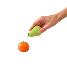 Een hand houdt een groen, peervormig Fluid Market Zout- en Pepervaatje vast boven een oranje, tomaatvormige shaker uit de Fluid Market Appelsien Peer 2 st. keramiekset - perfect voor een charmante tafelsetting.