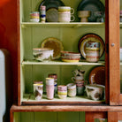 Een houten kast met groene planken toont een set HK Living 70s Ceramics Dessertkom Impression 4 st. kommen in aardetinten en abstracte patronen, netjes gerangschikt op twee planken.