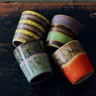 HK Living 70s Ceramics Koffiekoppen Layers, Mochi, Birthstone en Fierce liggend op een donkere houten ondergrond