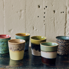 Zes HK Living 70s Ceramics Koffiekoppen op een donkere houten tafel: Zingy, Custard, Agave, Truffle, Gelato en Brew