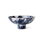 De HK Living 70s Ceramics Kom op Voet Indigo is een brede, ondiepe schaal van keramiek met een korte voet, voorzien van een blauw en wit gemarmerd patroon - een opvallend decoratief stuk van HK Living tegen een effen witte achtergrond.