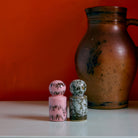 De HK Living 70s Ceramics Peper- en Zoutvaatje Baroque 2 st. set, met een roze en een bruine shaker, staat op een licht oppervlak voor een bruine kan en oranje wand - een gedurfd eerbetoon aan de vintage jaren 70 keramiekstijl.