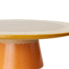 Een close-up van de HK Living 70s Ceramics Plateau/Taartschaal Papaya, een ronde keramieken standaard met een gele bovenkant en oranje gespikkelde onderkant, van HK Living, afgebeeld tegen een witte achtergrond.